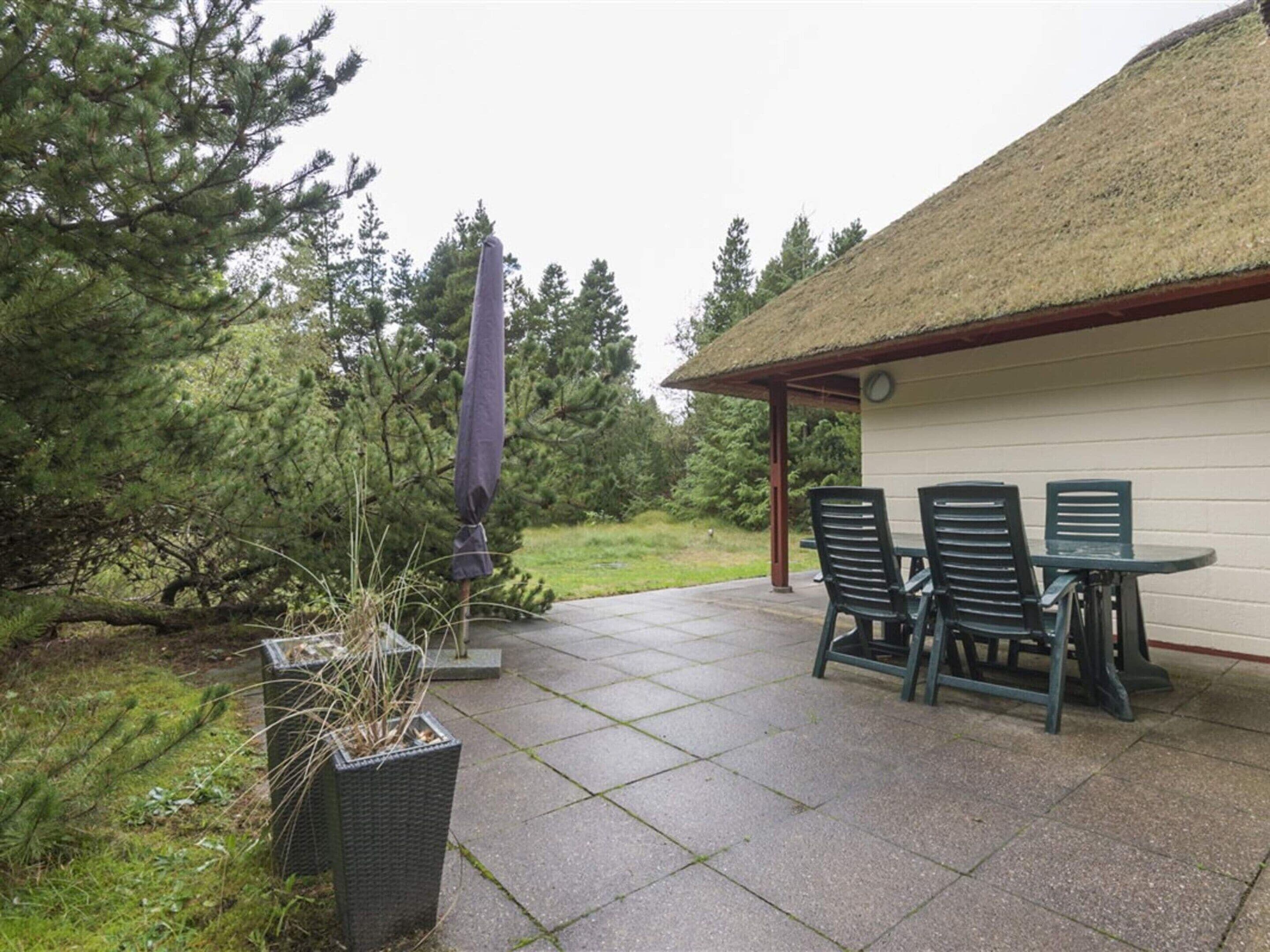 An outdoor patio with a table and chairs, surrounded by a thatched-roof structure and a potted plant.