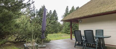 An outdoor patio with a table and chairs, surrounded by a thatched-roof structure and a potted plant.