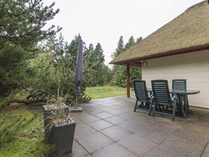 An outdoor patio with a table and chairs, surrounded by a thatched-roof structure and a potted plant. - 5 Star Holiday Home in Blavand (Blavand)
