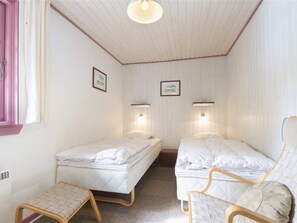 A small, single-room accommodation with two beds, a chair, a small table, and a window with curtains. - 5 Star Holiday Home in Blavand (Blavand)