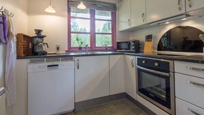 A kitchen with white cabinets, a microwave, a coffee maker, and a window with a view of greenery. - 5 Star Holiday Home in Blavand (Blavand)