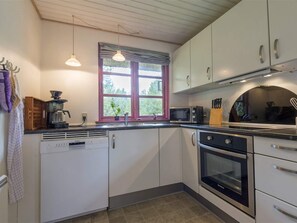 Eine Küche mit weißen Schränken, einer Mikrowelle, einer Kaffeemaschine und einem Fenster mit Blick auf Grünflächen.