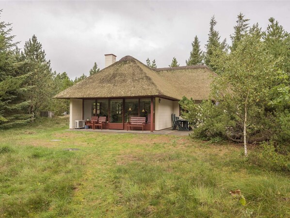 A single-story building with a thatched roof, a covered patio with seating, and a natural surrounding. - 5 Star Holiday Home in Blavand (Blavand)