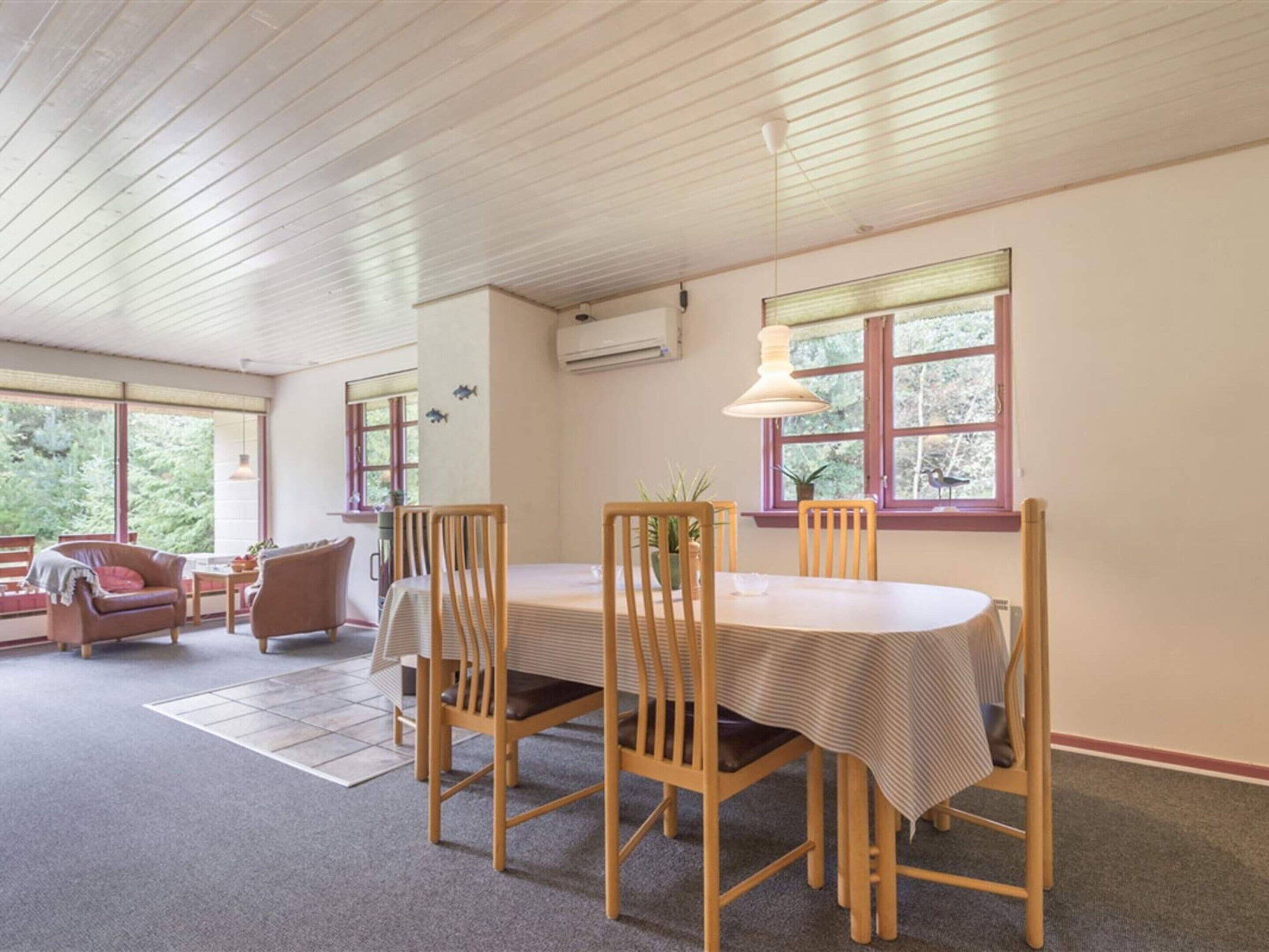 A dining area with a wooden table and chairs, a window with a view of greenery, and a ceiling with wooden beams.