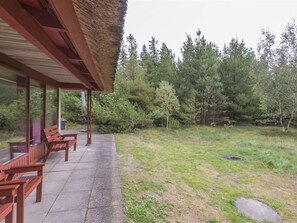 A covered outdoor seating area with benches, a thatched roof, and a view of a forested area. - 5 Star Holiday Home in Blavand (Blavand)