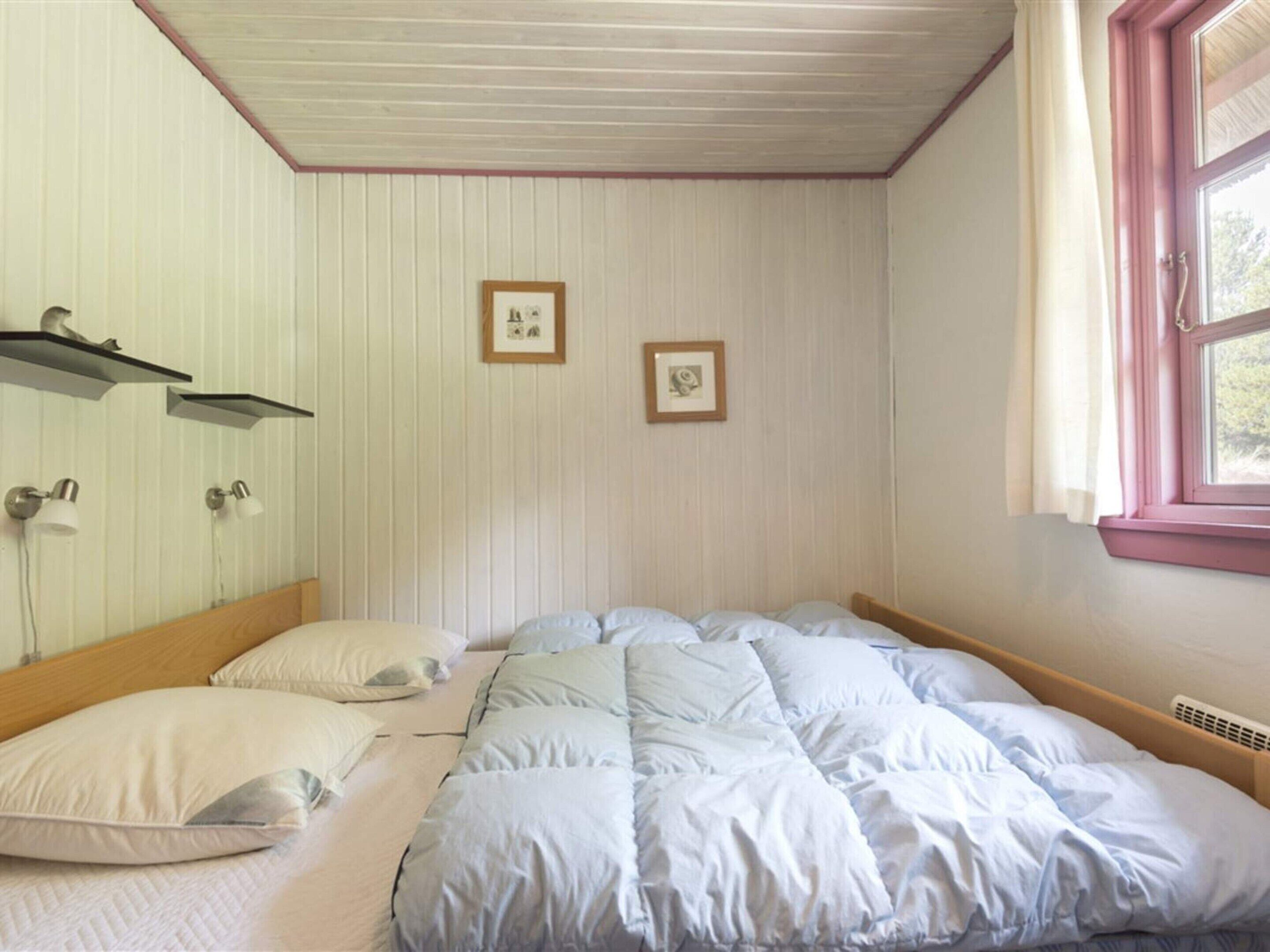 A bedroom with a bed, two wall-mounted lamps, and two framed pictures.