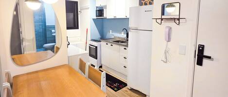 A compact kitchen with white cabinets, a microwave, and a stove. There is a wooden dining table with chairs and a large mirror above it.