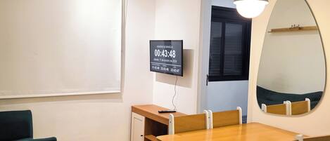 A room with a wooden table and chairs, a small cabinet, a television displaying a time, and a mirror on the wall.