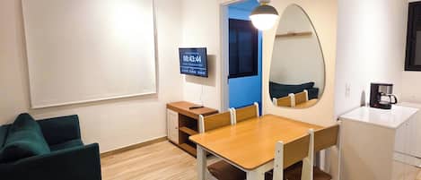 Una sala de estar moderna con comedor, televisor de pantalla plana, cafetera y un espejo grande.