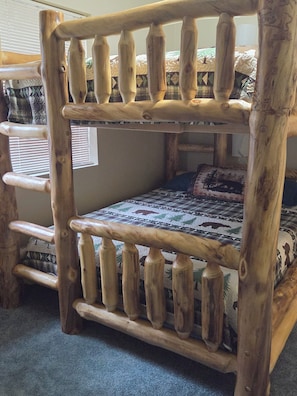 A bunk bed with a wooden frame and a quilt with a forest and animal pattern.