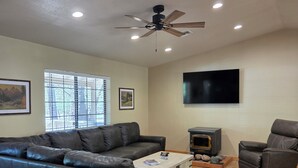 A living room with a sectional sofa, a fireplace, a television, and a ceiling fan. - Husky Bear Retreat - Beautiful house in the tall pines of Pinetop Lakeside (Pinetop-Lakeside)
