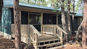 A cabin with a wooden deck and stairs leading to a porch, surrounded by trees.