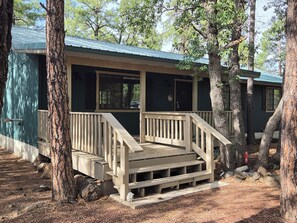 A cabin with a wooden deck and stairs leading to a porch, surrounded by trees.