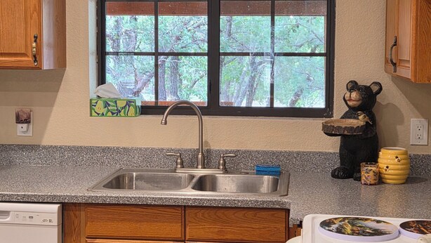 A kitchen with wooden cabinets, a granite countertop, a sink, a window with a view of trees, and a bear figurine on the counter. - Husky Bear Retreat - Beautiful house in the tall pines of Pinetop Lakeside (Pinetop-Lakeside)