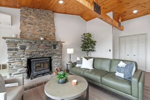 Una sala de estar con chimenea de piedra, un sofá verde, una mesa de centro redonda y una planta en maceta.