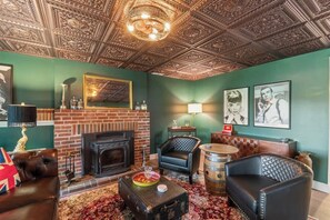 A room with a fireplace, leather furniture, a patterned rug, and a decorative ceiling. - Lakeview House: Hot Tub, Speakeasy, Firepit, Gameroom (Hammondsport)