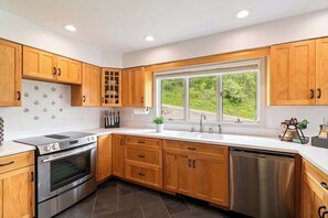 Una cocina moderna con armarios de madera, electrodomésticos de acero inoxidable y un amplio ventanal con vistas a la vegetación.