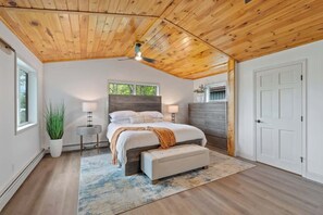 Un dormitorio con techo de madera, una cama con reposabajera, lámparas de noche, una ventana y una puerta.