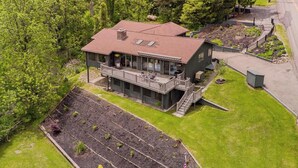 A two-story house with a balcony, surrounded by a well-maintained lawn and trees. - Lakeview House: Hot Tub, Speakeasy, Firepit, Gameroom (Hammondsport)