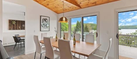 A dining area with a wooden table and chairs, a pendant light, and a view of a deck and landscape.