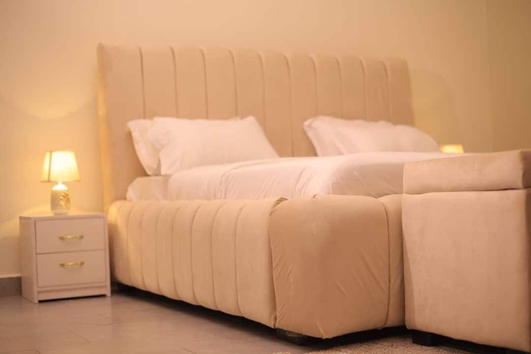 Uma cama com cabeceira, mesa de cabeceira com gavetas e um abajur.