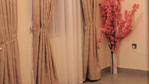 A room with beige curtains, a sheer curtain, and a pink artificial plant. - NJ Homes Bunga  (Kampala)