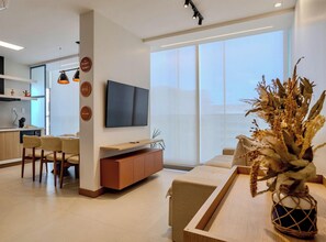 A modern living room with a flat-screen TV, a dining area, and a kitchen in the background. - 2 Bedroom with Sea View Near Farol da Barra (Salvador)