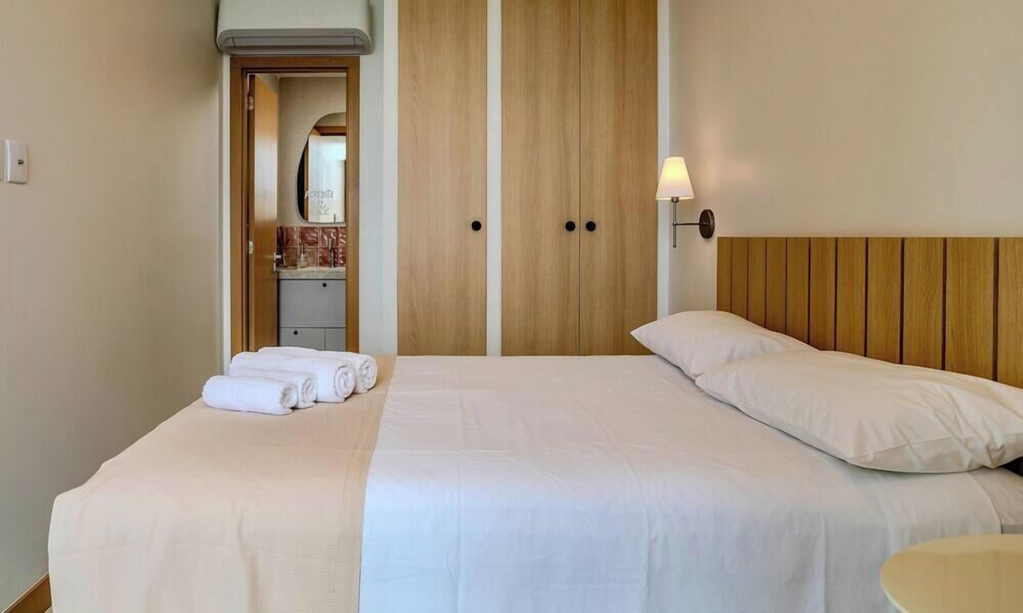 A hotel room with a bed, a nightstand, a lamp, and a wardrobe.
