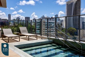 A rooftop pool with a glass balustrade, lounge chairs, and a view of the city skyline. - 2 Bedroom with Sea View Near Farol da Barra (Salvador)