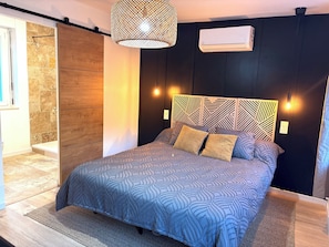 A modern bedroom with a patterned bedspread, a wooden headboard with geometric patterns, and a hanging light fixture. - Le Mocopek Vacation Rental (sleeps 5) (Bolbec)