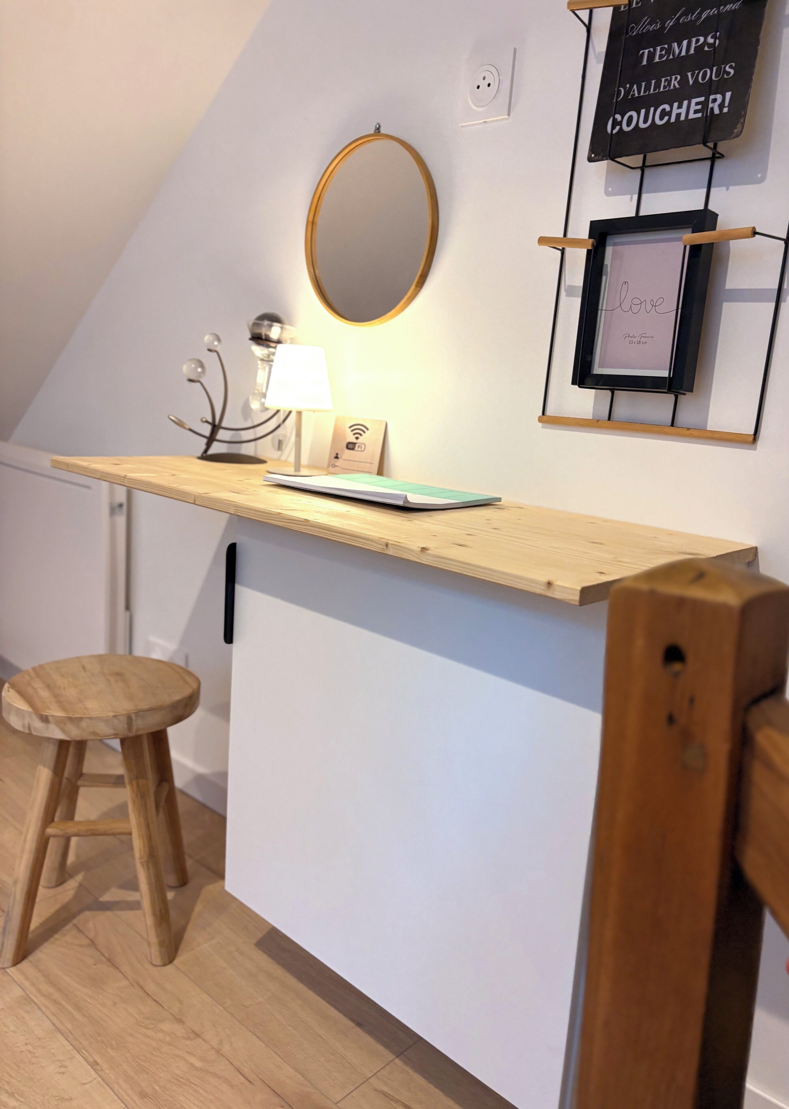 Ett litet, modernt pentry med en träbänkskiva, en pall, en spegel och en vägghängd hylla med en skylt.