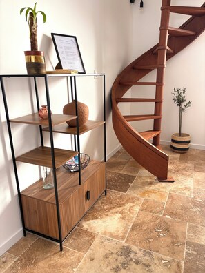 A wooden spiral staircase, a metal shelving unit with a vase and a framed certificate, and a small potted plant. - Le Mocopek Vacation Rental (sleeps 5) (Bolbec)