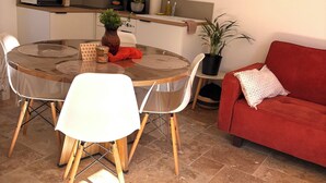 A compact living space with a dining table, chairs, a red sofa, and a kitchen area with cabinets and appliances. - Le Mocopek Vacation Rental (sleeps 5) (Bolbec)