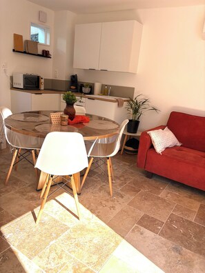 A compact living space with a dining table, chairs, a red sofa, and a kitchen area with cabinets and appliances. - Le Mocopek Vacation Rental (sleeps 5) (Bolbec)