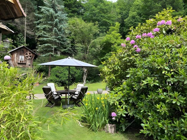 Ein Garten mit einer Holzkonstruktion, einem Tisch mit Stühlen und verschiedenen Pflanzen.