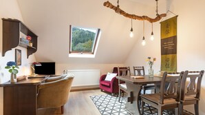 A cozy room with a dining table, chairs, a television, a window with a view of trees, and a decorative hanging light fixture.