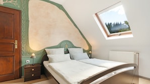 A bedroom with a sloped ceiling, a bed with a headboard, a nightstand, a lamp, and a window with a view of trees.