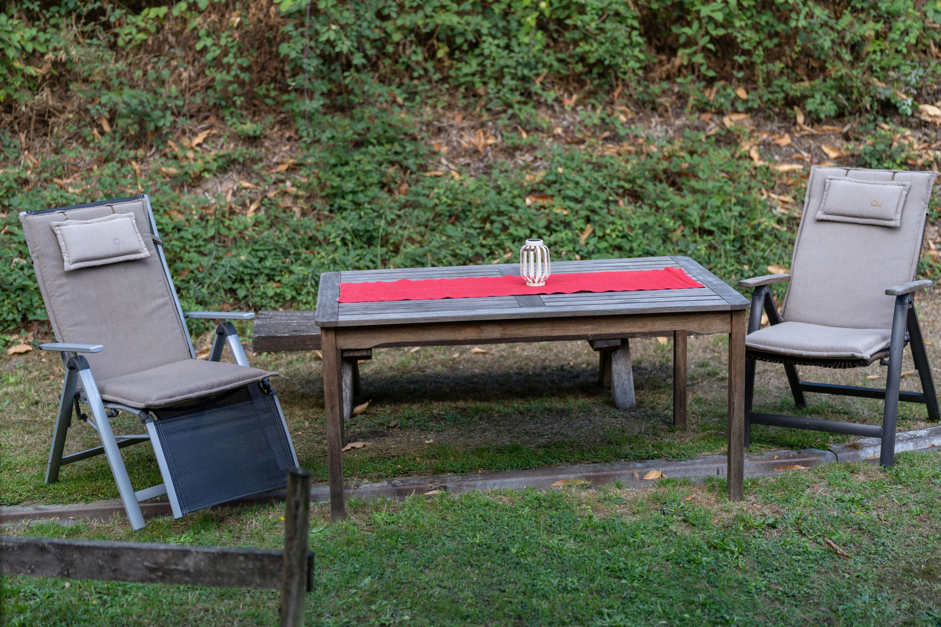 An outdoor seating area with two chairs and a table, surrounded by greenery.