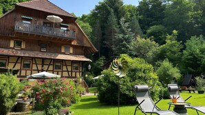 A wooden chalet with a balcony, surrounded by lush greenery and a garden with flowers.