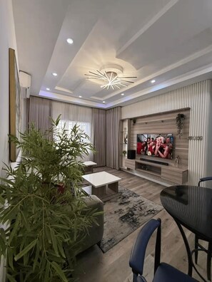 Ein modernes Wohnzimmer mit Fernseher, Couchtisch, Esstisch und einer großen Pflanze.