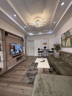 A modern living room with a flat-screen TV, a sofa, a coffee table, and a dining area with chairs. - Lovely 1-Bedroom Apartment in Lekki 1 with Fast Wi-Fi & 24/7 Power (Lagos)