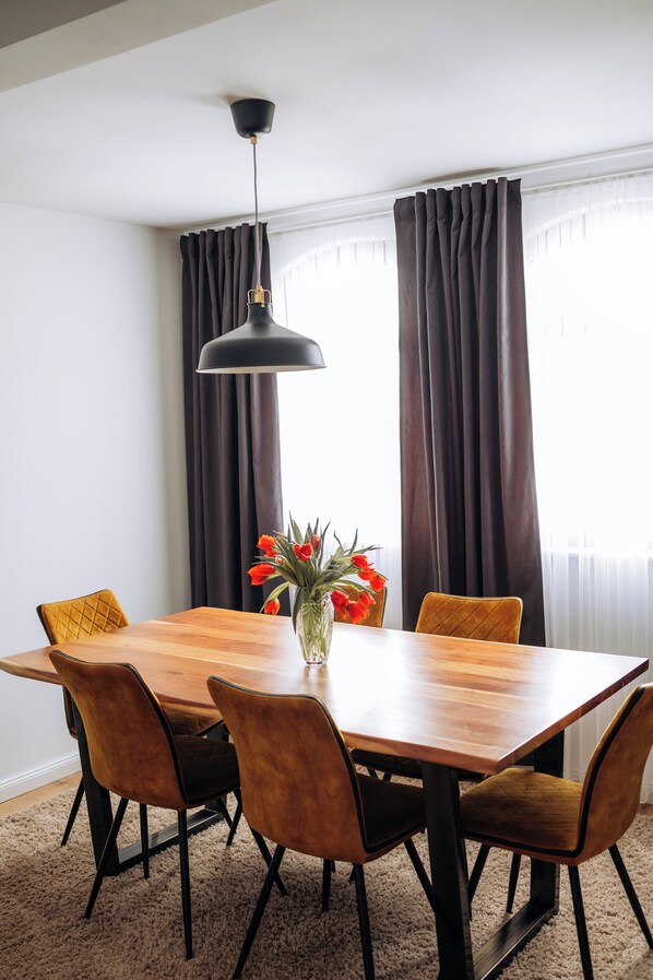 Een eetgedeelte met een houten tafel, vier stoelen, een bloemenvaas en een hanglamp.
