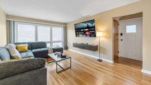 A living room with a sofa, coffee table, TV, and a door. - Spacious Modern Duplex | Minutes from NYC (Bayonne)