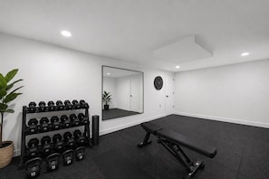 Un gimnasio con una banca, mancuernas y pesas de kettlebell.