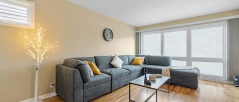 Un salon moderne avec un canapé d’angle, une table basse et un arbre décoratif.