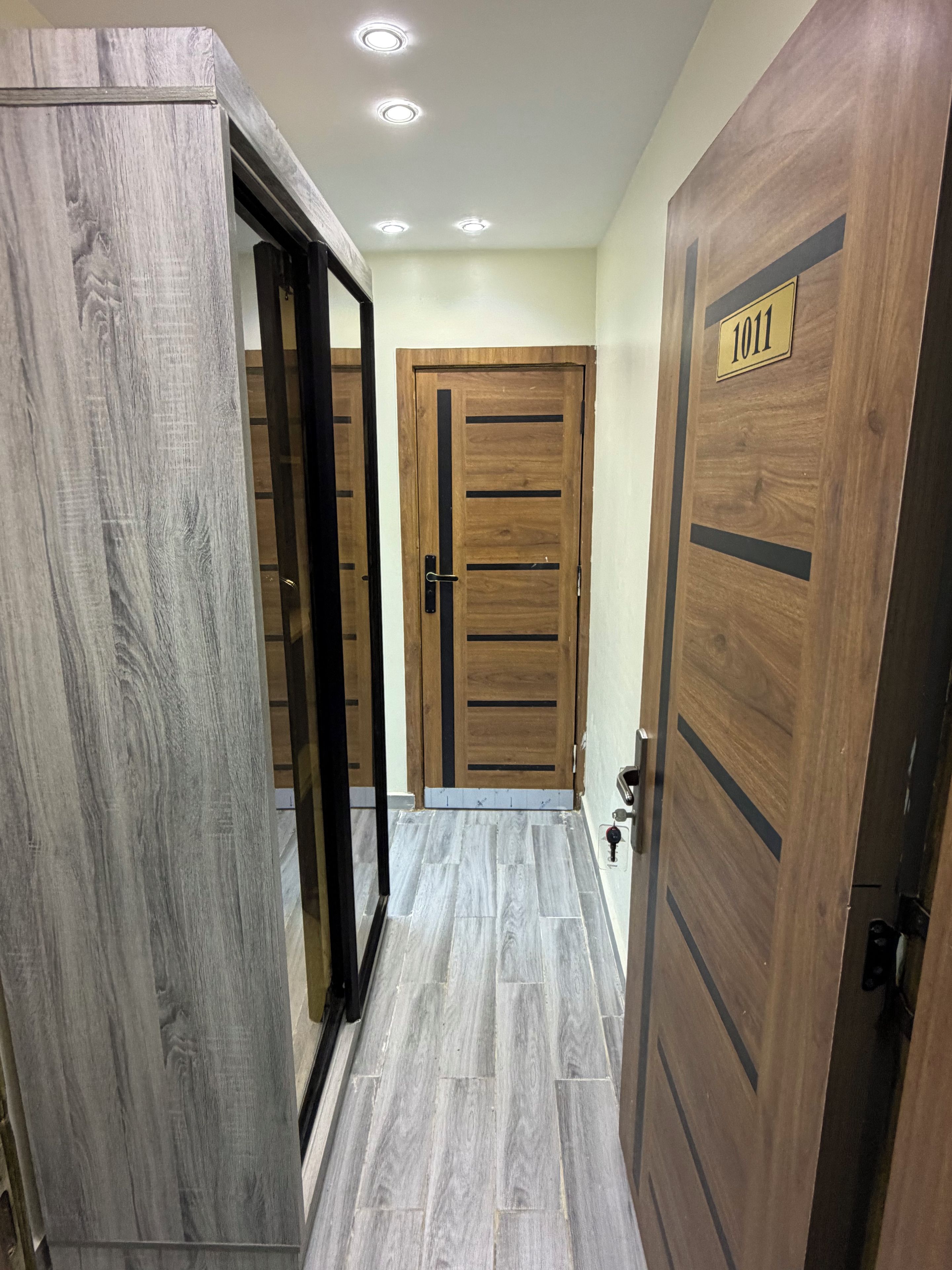 Un pasillo con puertas de madera, piso de baldosas y luces empotradas en el techo.
