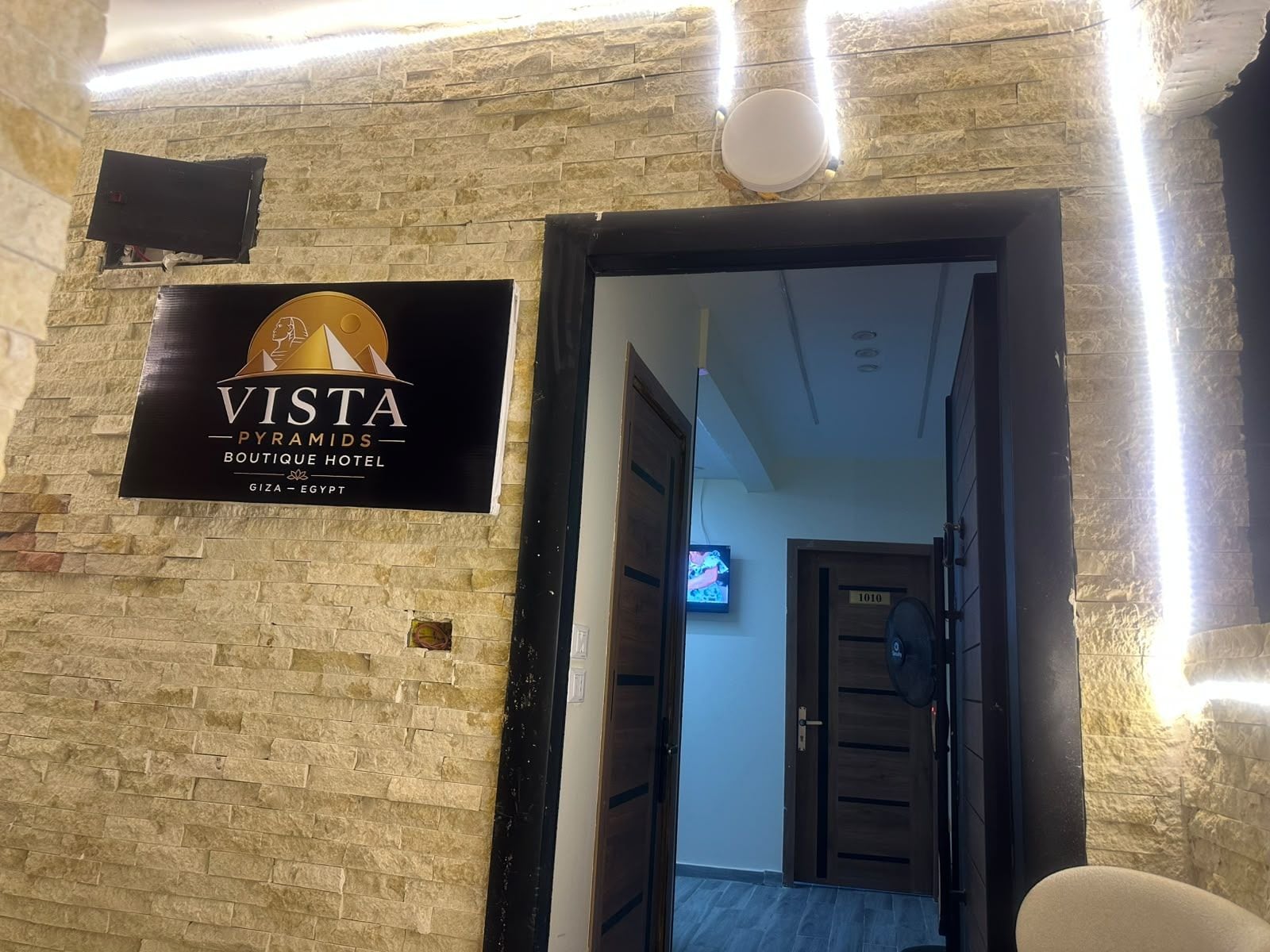 A hotel entrance with a sign for 'VISTA Pyramids Boutique Hotel' and a television in the background.