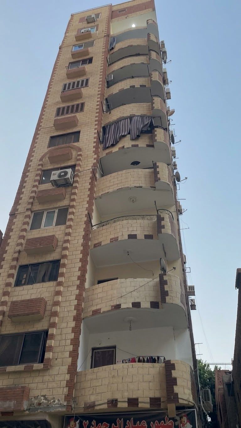 Un edifici residencial de diversos pisos amb balcons, antenes parabòliques i un cel serè.