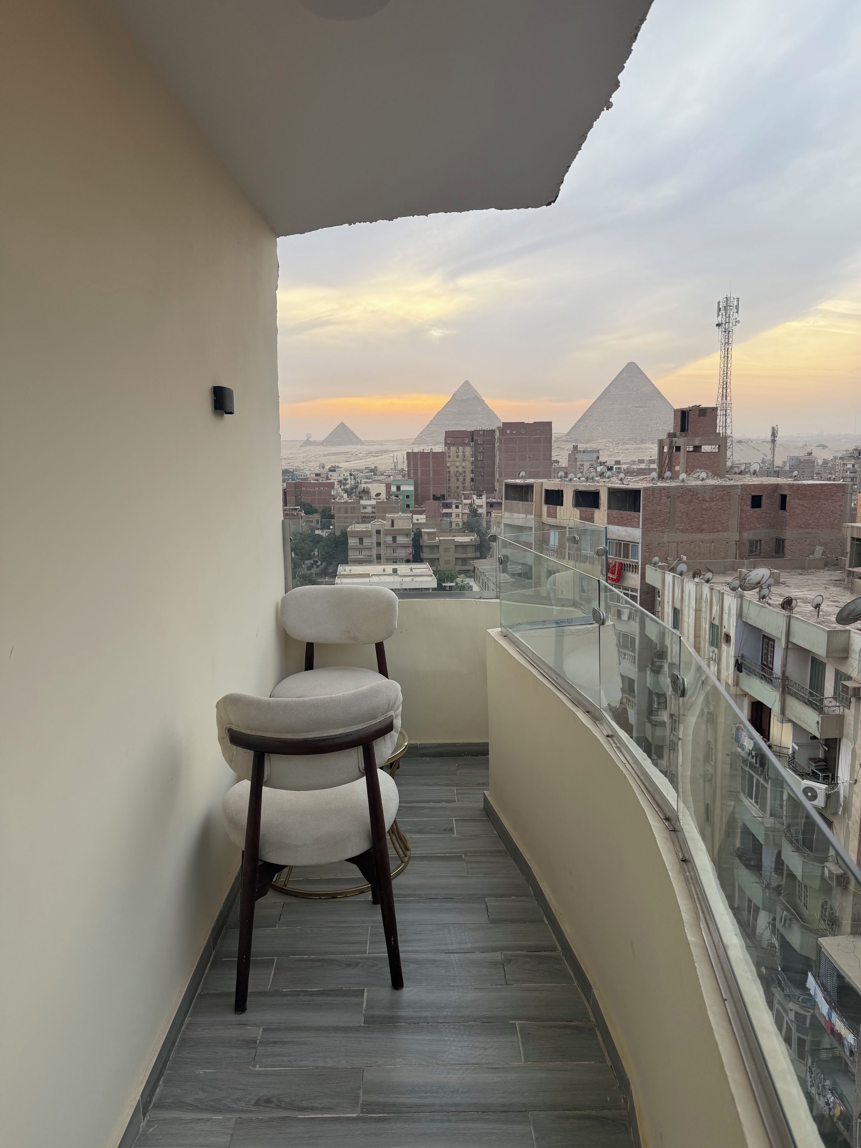 Een balkon met een stoel, een glazen hekwerk en een uitzicht op piramides in de verte.