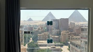 Vista desde una ventana de un paisaje urbano con edificios y pirámides al fondo.